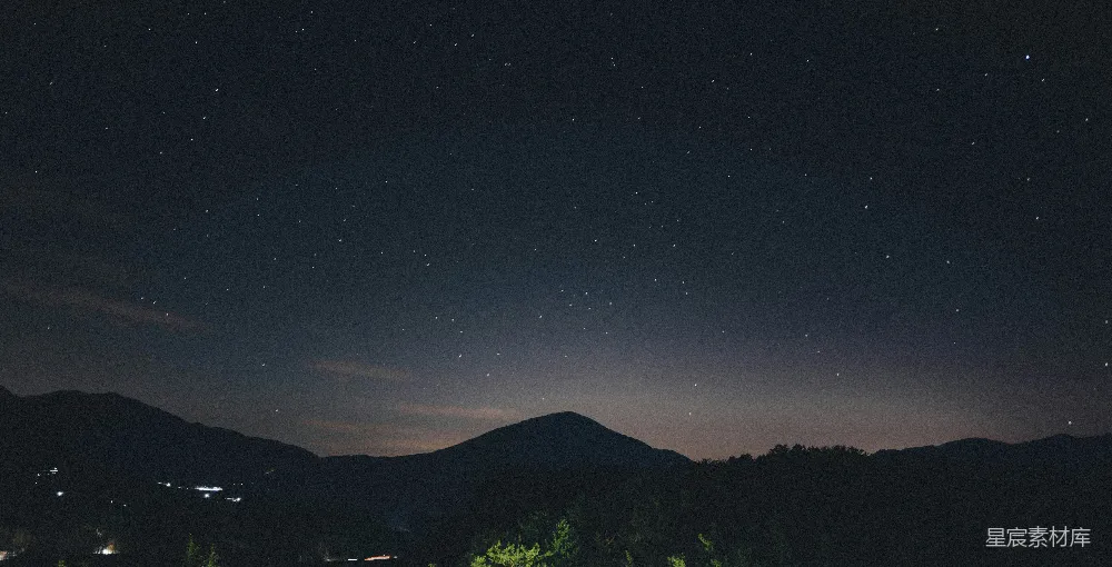 这张图片展示了一个宁静的夜晚，夜空中布满了星星，山峦在黑暗中若隐若现。远处可以看到一些微弱的灯光，营造出一种静谧而神秘的氛围。适合用作自然风光的背景图，传达出一种远离喧嚣、回归自然的感觉。