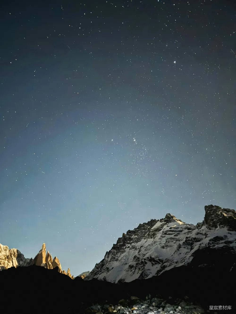 这张图片展示了夜晚星空下的壮丽雪山。天空中点缀着无数闪烁的星星，与下方被月光映照的雪山形成鲜明对比。整个画面充满了宁静与神秘的氛围，适合用作自然风光或夜景主题的背景素材。