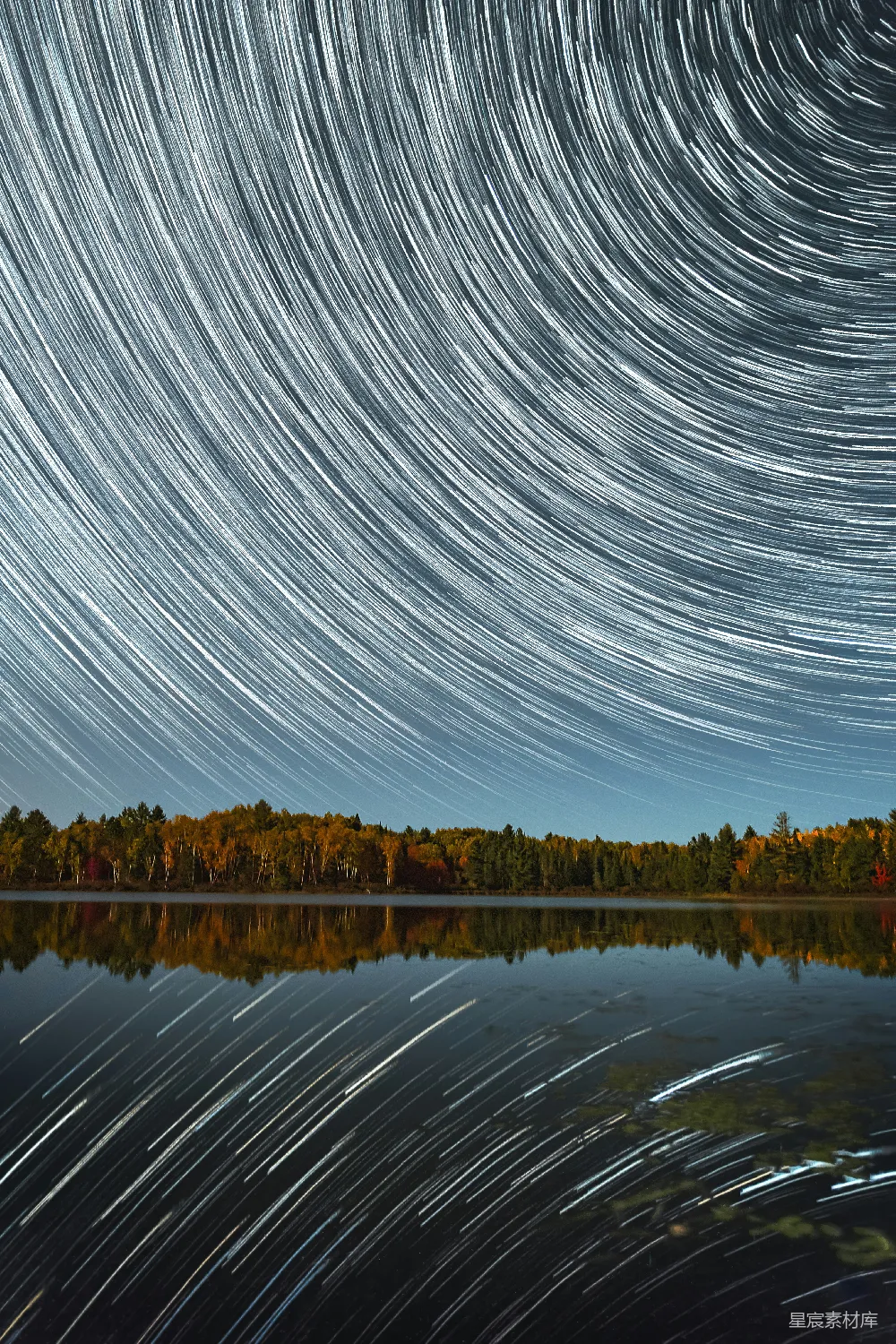 这张图片展示了一个宁静的夜景，湖面倒映着天空中的星轨，形成了美丽的对称效果。远处的森林在湖面上清晰地反射，增添了画面的深度和宁静感。这种景象通常会在长时间曝光摄影中捕捉到，展示了大自然的神秘和美丽。