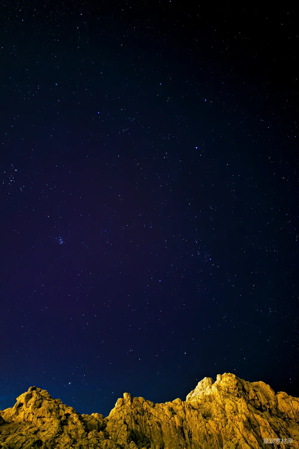 这张图片展示了夜晚的天空，满天繁星点缀在深蓝色的夜幕上，岩石在前景中呈现出温暖的黄色光晕，营造出宁静而神秘的氛围。适合用作自然风光、星空和宁静等主题的背景或素材。