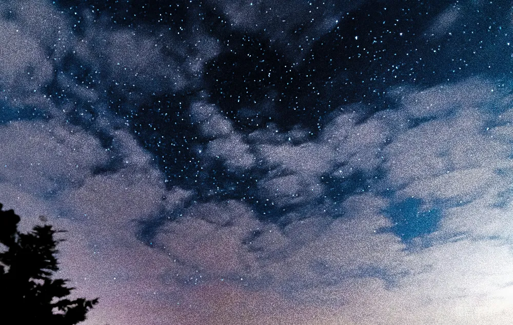 这张图片展示了夜空中繁星点点的景象，云朵悠然飘动，营造出一种宁静而梦幻的氛围。适合用作自然风光的背景，或是表达内心宁静与梦想的主题。