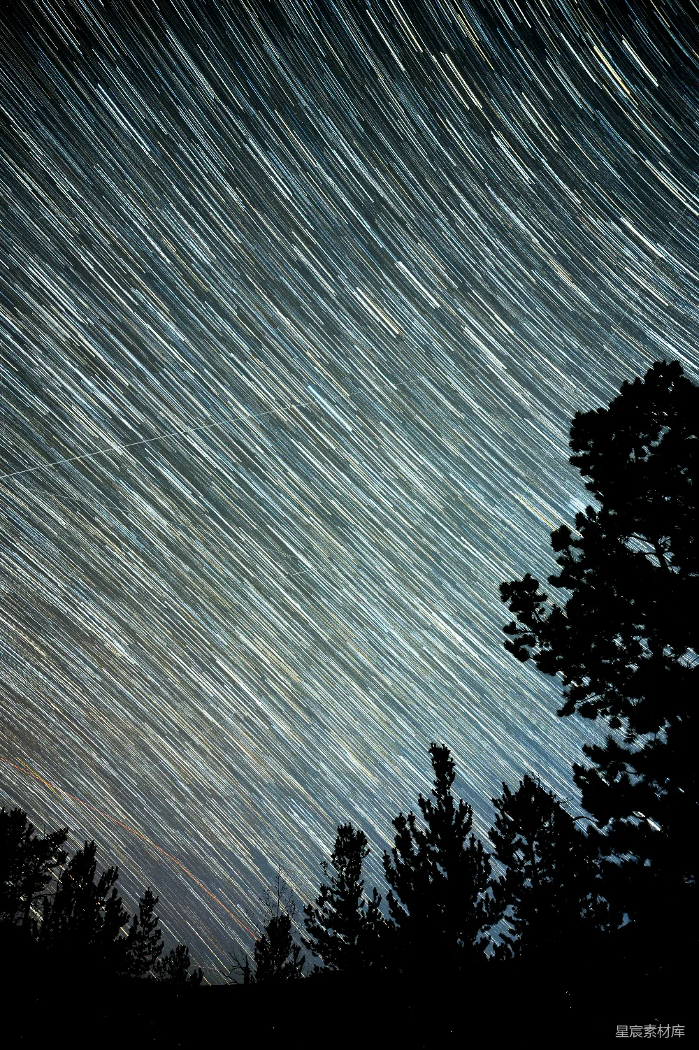 这张照片展示了夜空中的星轨效果，星星的轨迹清晰地形成了无数条平行线，背景是深邃的夜色和剪影的树木。这幅图像捕捉到了自然与宁静的完美结合，适合用作自然风光或摄影爱好者的素材。