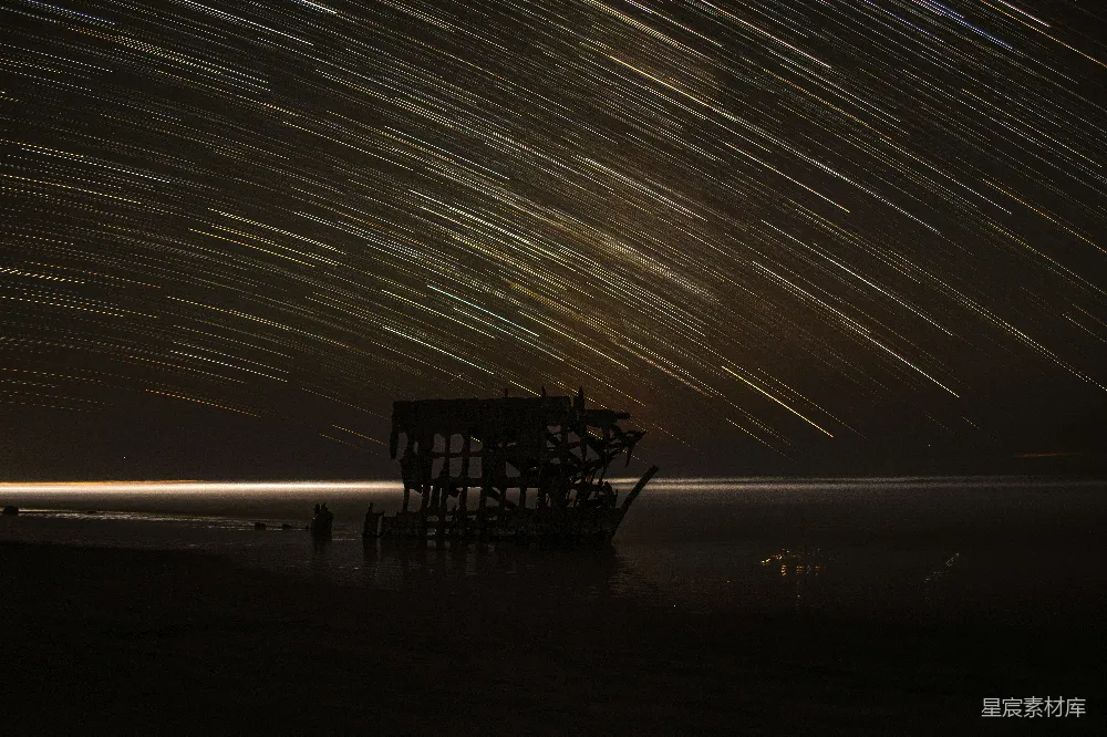 这张图片展示了一艘被淹没在水中的废弃船骸，夜空中布满了星轨，形成了美丽的光带效果。背景的海面上泛着微光，整个场景显得既神秘又宁静。这幅作品适合用作自然风光、夜晚景观或废弃建筑主题的背景素材。