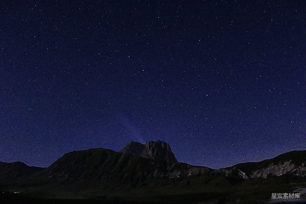 这张图片展示了在星空下山峰的剪影。深蓝色的夜空中点缀着无数闪烁的星星，山峰的轮廓在黑暗中显得格外醒目。这幅图像传达了一种宁静和神秘的氛围，适合用作自然风光、旅行宣传或静谧夜晚主题的背景。