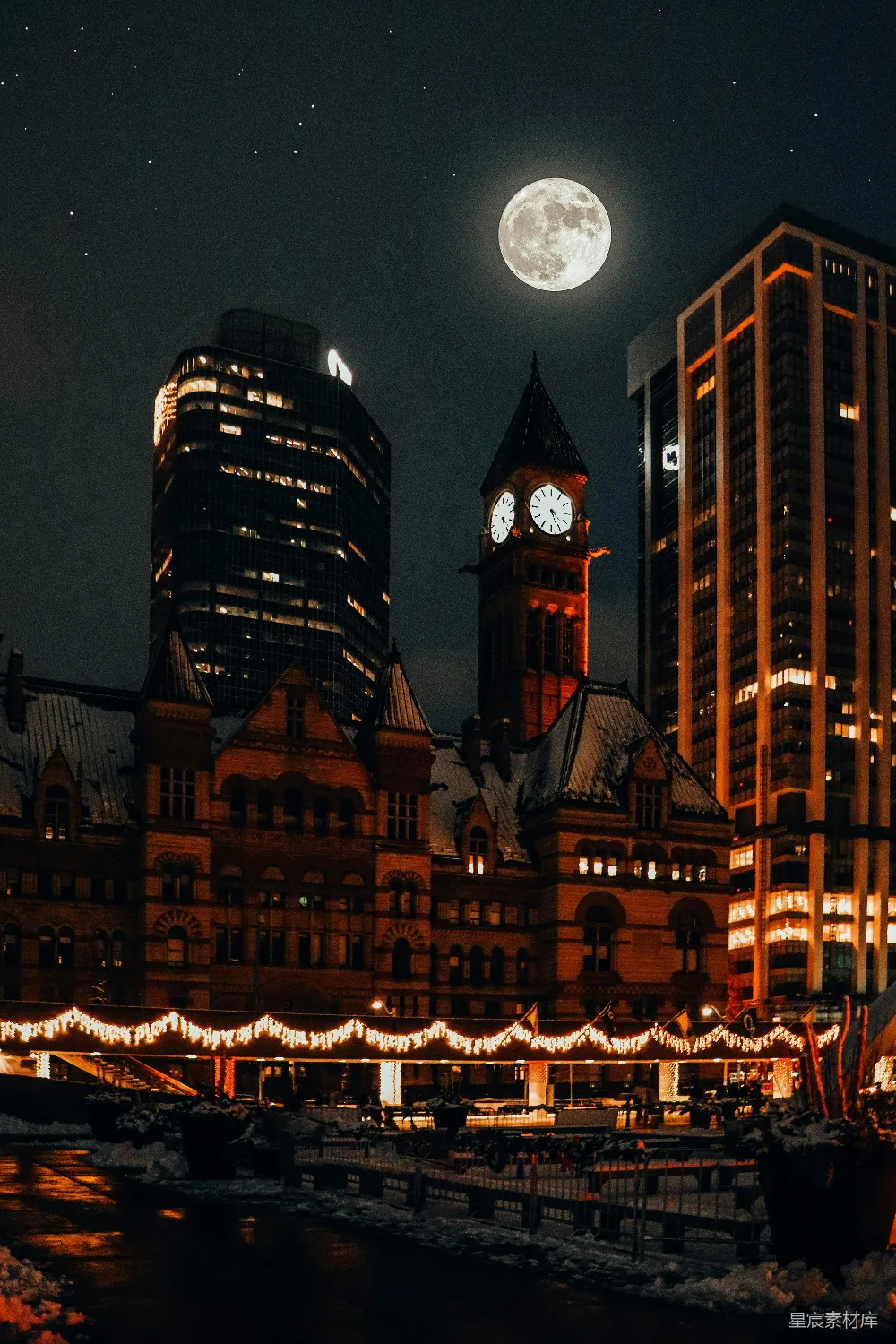 这张图片展示了一个城市的夜景，月亮高挂在夜空中，照亮了城市的建筑。前景是一座古老的钟楼，背景是现代的摩天大楼，地面上覆盖着雪，街道两侧装饰着灯光，营造出一种宁静而美丽的氛围。
