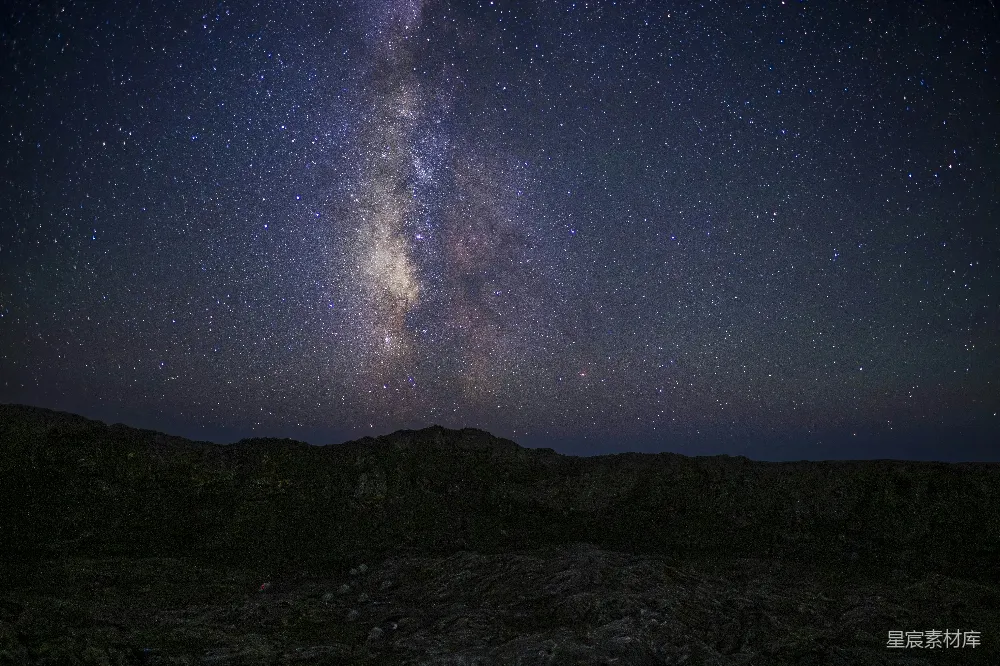这张图片展示了一片广阔的夜空，银河清晰可见，星星点缀其间。地平线下的岩石地形在黑暗中若隐若现，营造出一种宁静而神秘的氛围。适合用于自然风光、天文摄影或宁静氛围的场景。