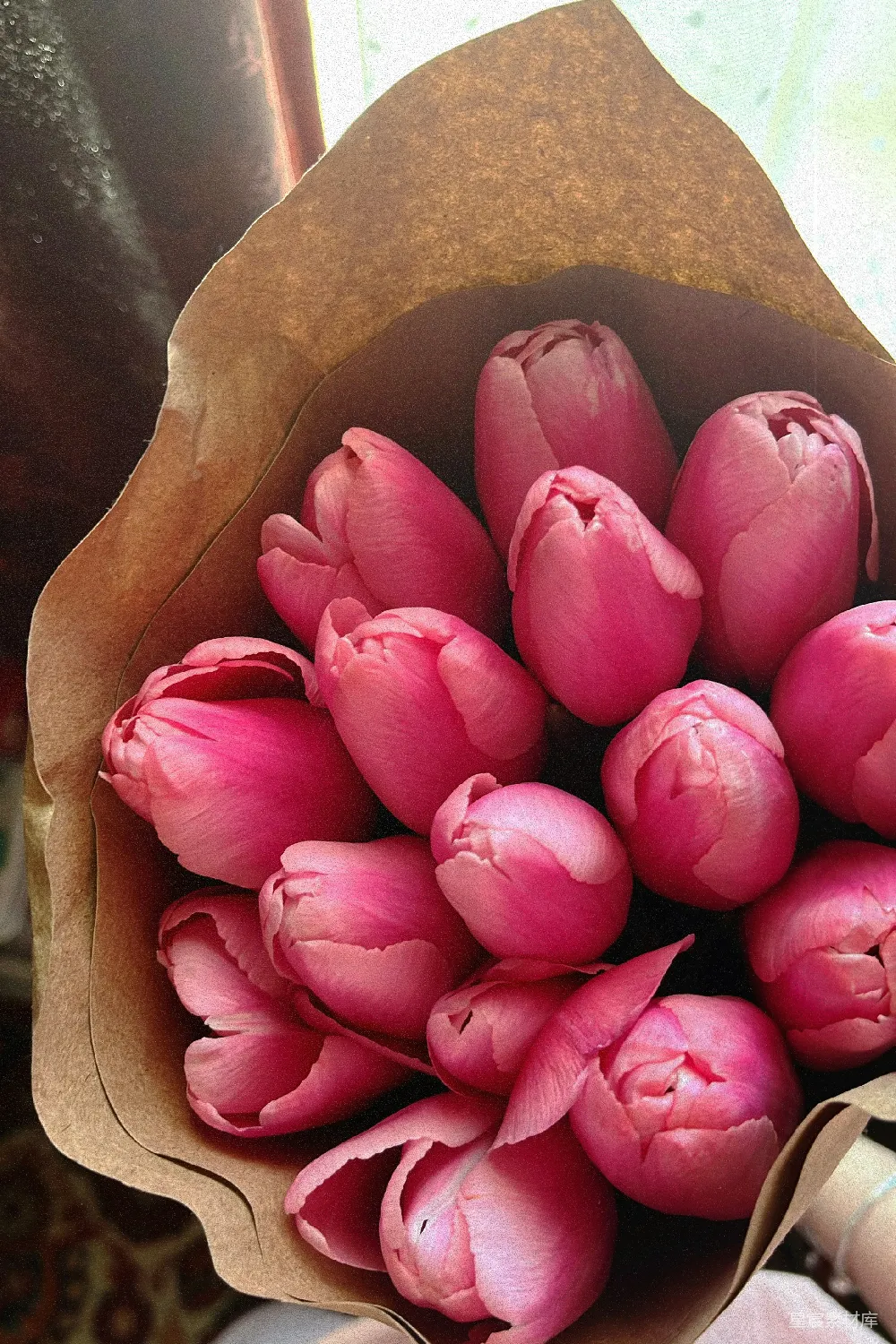 这是一束粉红色的郁金香花束，花瓣层层叠叠，显得非常优雅和浪漫。花束被包裹在棕色的纸中，为整体增添了一丝质朴的美感。这种花束非常适合用来表达爱意和感谢之情，适合在婚礼、情人节或生日等特殊场合使用。