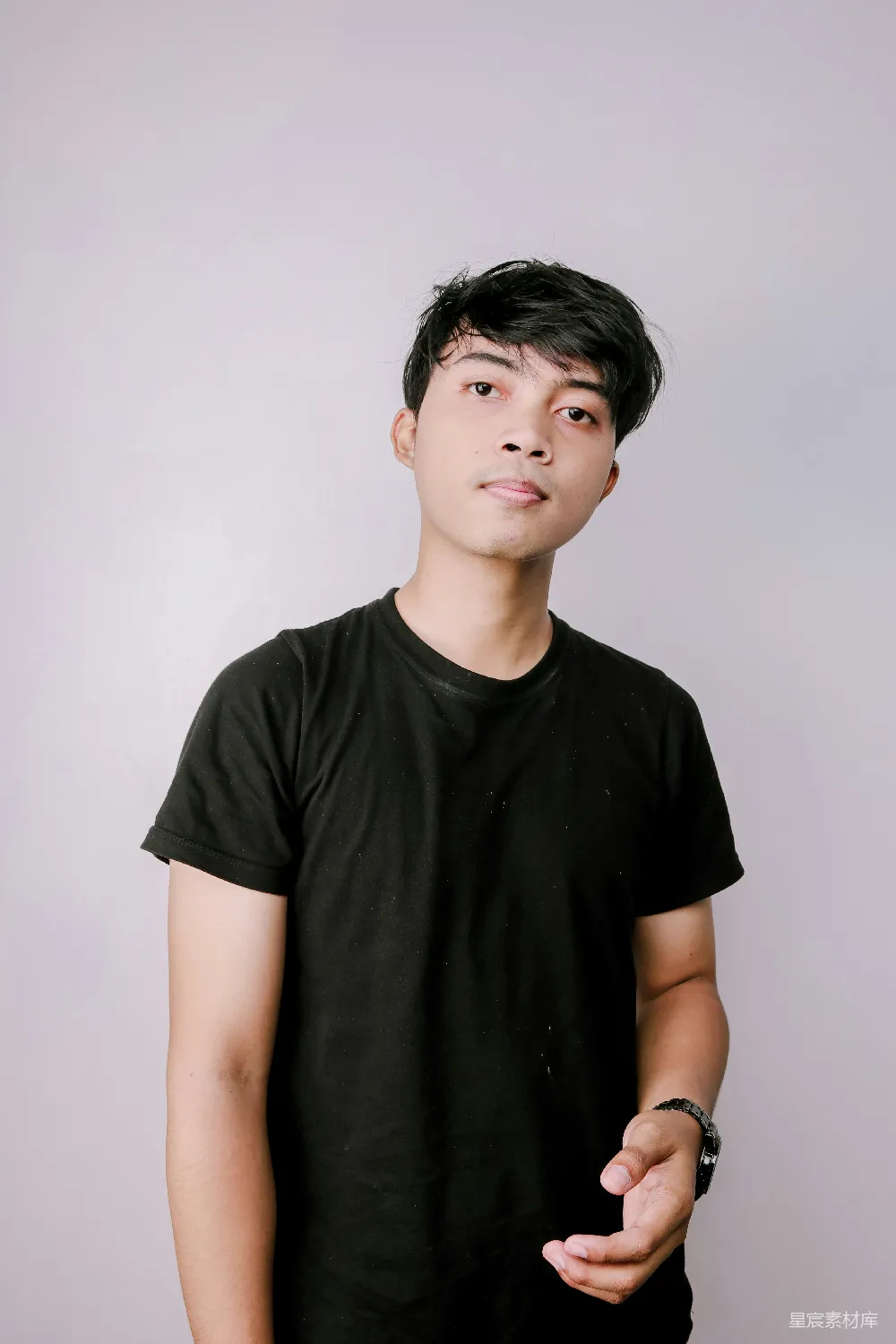 图片中是一位年轻男子，他穿着简单的黑色T恤，背景简洁，光线柔和，营造出一种自然、清新的氛围。男子面带微笑，右手微微举起，展现出一种自信和放松的态度，适合用于表现青春活力、自信和自然风格的主题。