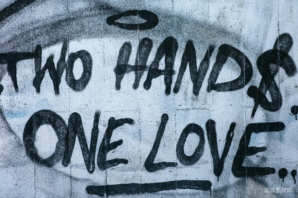 这幅涂鸦作品以‘Two Hands, One Love’为主题，表达了团结和爱的深刻含义。文字以粗犷的涂鸦艺术形式呈现，背景为灰色的水泥墙面，给人一种强烈的视觉冲击。这种风格的涂鸦常用于表达社会信息，激励人们团结一致，共同面对挑战。适合用作