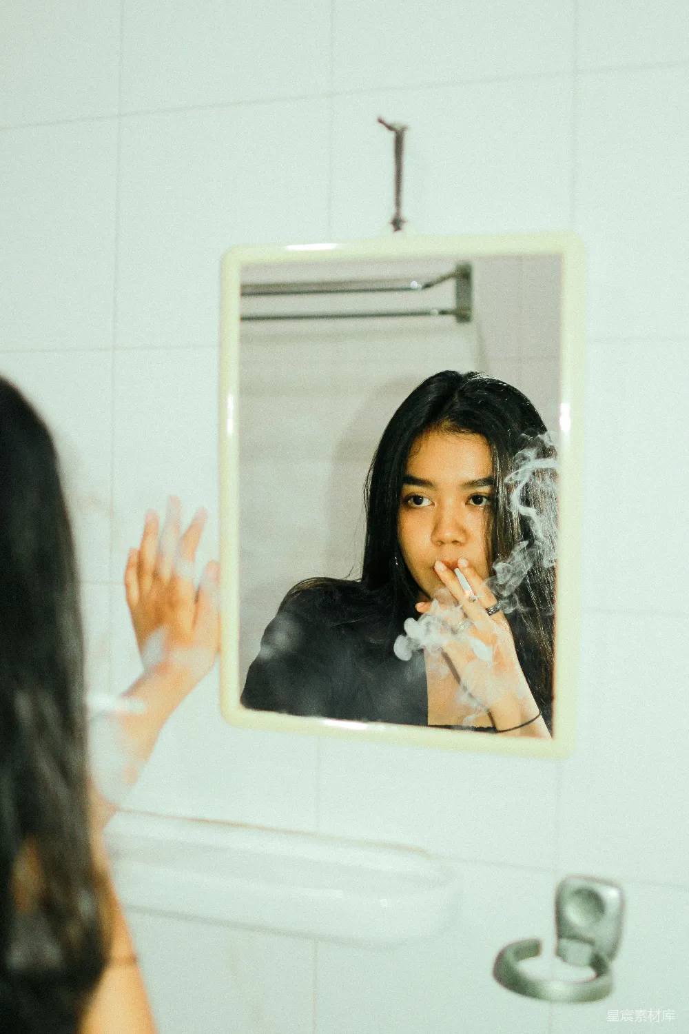 这张图片捕捉到了一个人在浴室镜子前的瞬间，手中握着烟，镜子上弥漫着烟雾，营造出一种孤独与沉思的氛围。场景充满了艺术感，适合用作表达内心情感或自我反思的素材。