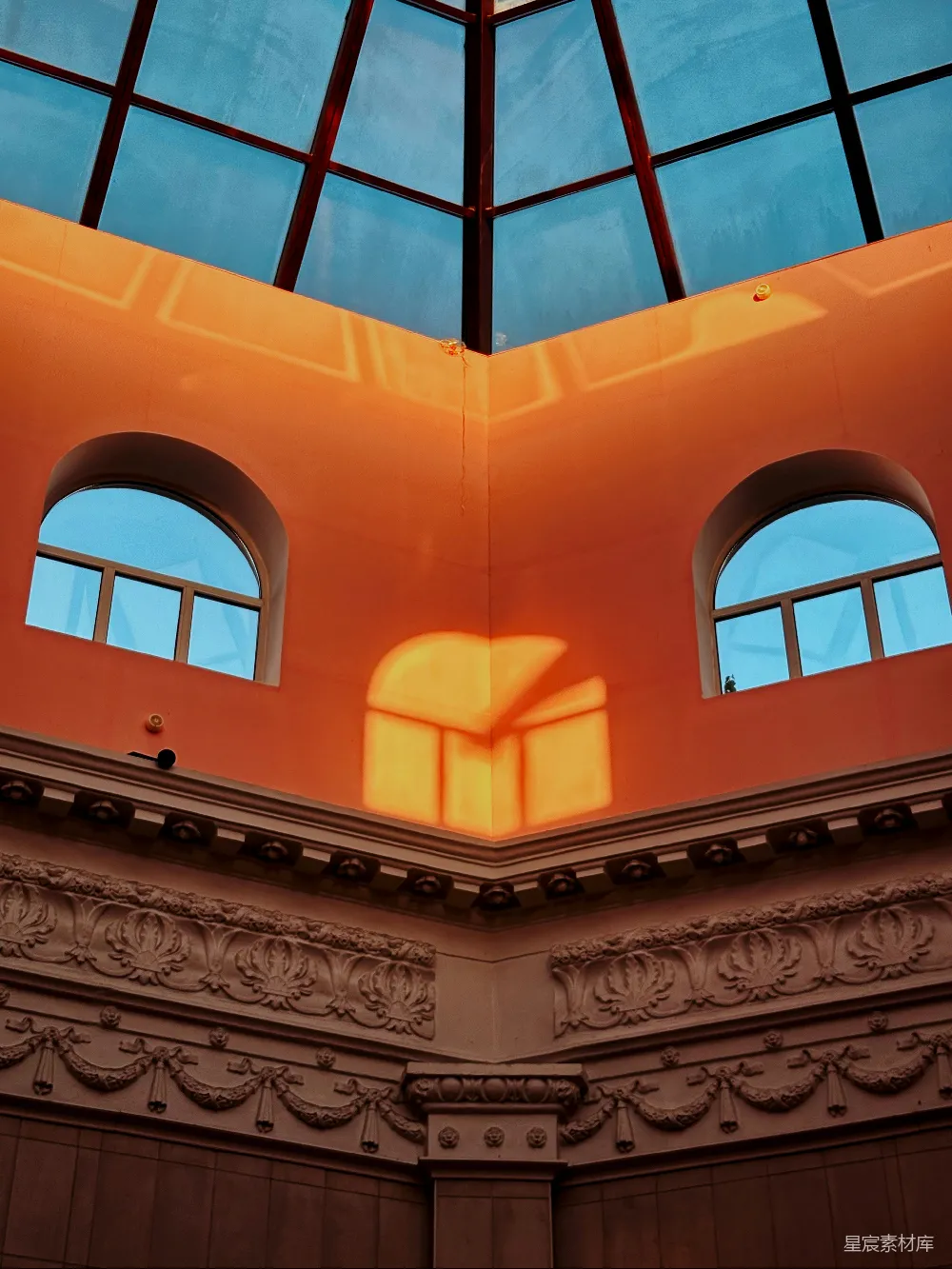 这张图片展示了一个温暖的阳光洒在建筑角落的情景。橙色的墙壁和窗框形成了鲜明的对比，阳光照射在建筑的角落，投射出柔和的光影，营造出一种宁静而温暖的氛围。适合用于展示建筑的细节、光线的运用以及温暖的色调。