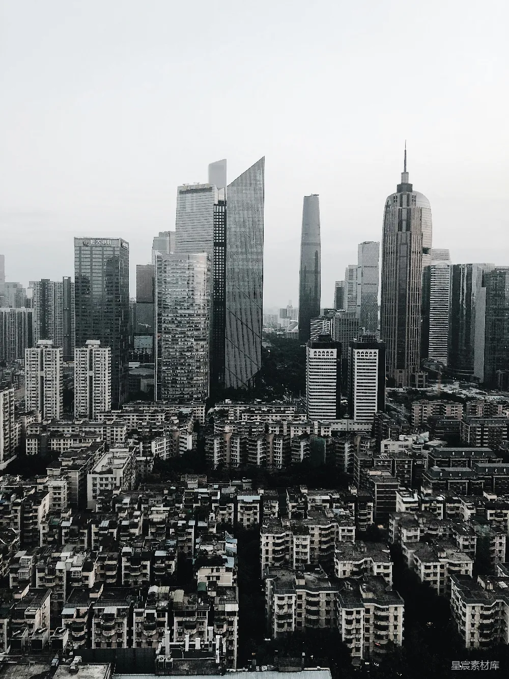 这张图片展示了城市中高楼大厦的黑白对比。背景中的现代化高楼与前景中密集的低层住宅形成鲜明对比，突显了城市化进程与旧城区的并存。整体画面简洁，色调统一，适合用于城市发展的主题素材。