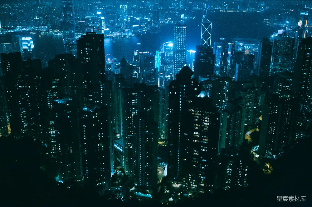 这张图片展示了一座城市的夜景，整体色调为蓝绿色。画面中高楼大厦林立，灯光点缀其间，展现出繁忙都市的夜晚景象。远处的水域反射着灯光，增添了一份宁静与美丽。适合用于城市夜景、旅游宣传、都市生活等场景。