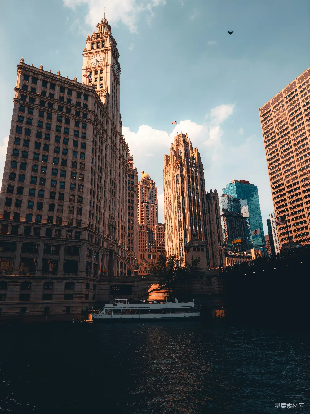 这张图片展示了芝加哥的天际线，包括著名的Wrigley Building和Chicago River。阳光洒在建筑物上，形成美丽的光影效果。河上的游船为这幅城市风景增添了一丝生活气息。