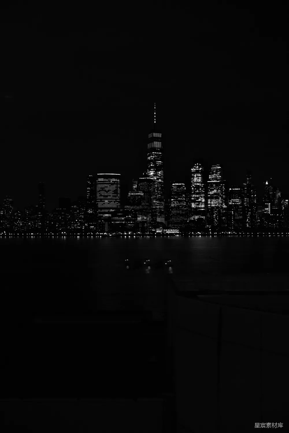 这张图片展示了一个城市的夜景，主要以黑白色调呈现，突出了城市的建筑轮廓和灯光。背景中的摩天大楼在黑暗中显得格外醒目，而前景的水面则反射出城市的轮廓。整体画面简洁而富有艺术感，适合用作城市风光或夜间摄影的素材。