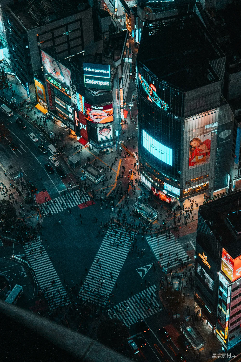 这张图片展示了东京繁忙的十字路口夜景。灯光璀璨，广告牌闪烁，行人和车辆在十字路口穿梭，构成一幅现代都市的繁忙景象。高楼大厦的玻璃幕墙反射着夜空的光辉，营造出一种繁华而充满活力的氛围。