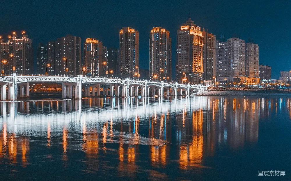 这张图片展示了夜晚城市的景象，一座桥梁横跨河流，河面上倒映出城市的灯光，形成美丽的光影效果。城市的高楼大厦灯火辉煌，展现出现代都市的繁华与活力。适合用于展示城市夜景、都市生活或是现代建筑的视觉效果。