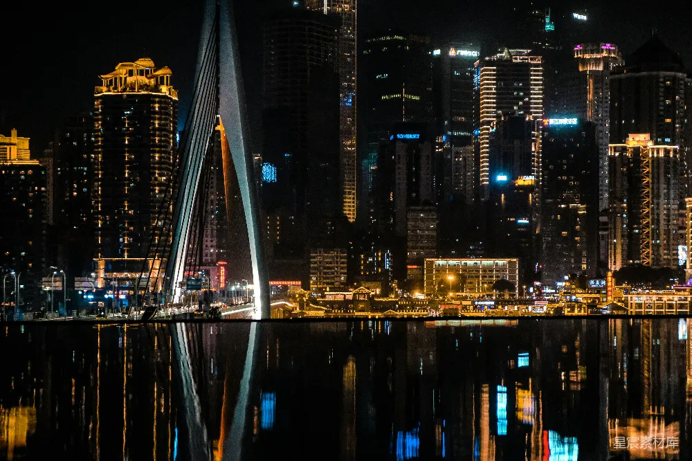 这张图片展示了一个城市的夜景，桥梁的倒影在水面上形成美丽的对称，远处的高楼大厦灯火辉煌，营造出一种繁华而宁静的氛围。适合用作城市夜景、现代建筑或都市生活的背景图。