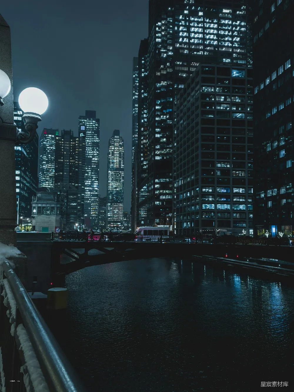 图片展示了一座城市的夜景，河岸边的桥梁和远处灯火辉煌的高楼大厦相映成趣。天空中飘着一层薄雾，河面上反射着城市的灯光，营造出一种宁静而又繁华的氛围。适合用作城市夜景的背景图或城市风光的展示。