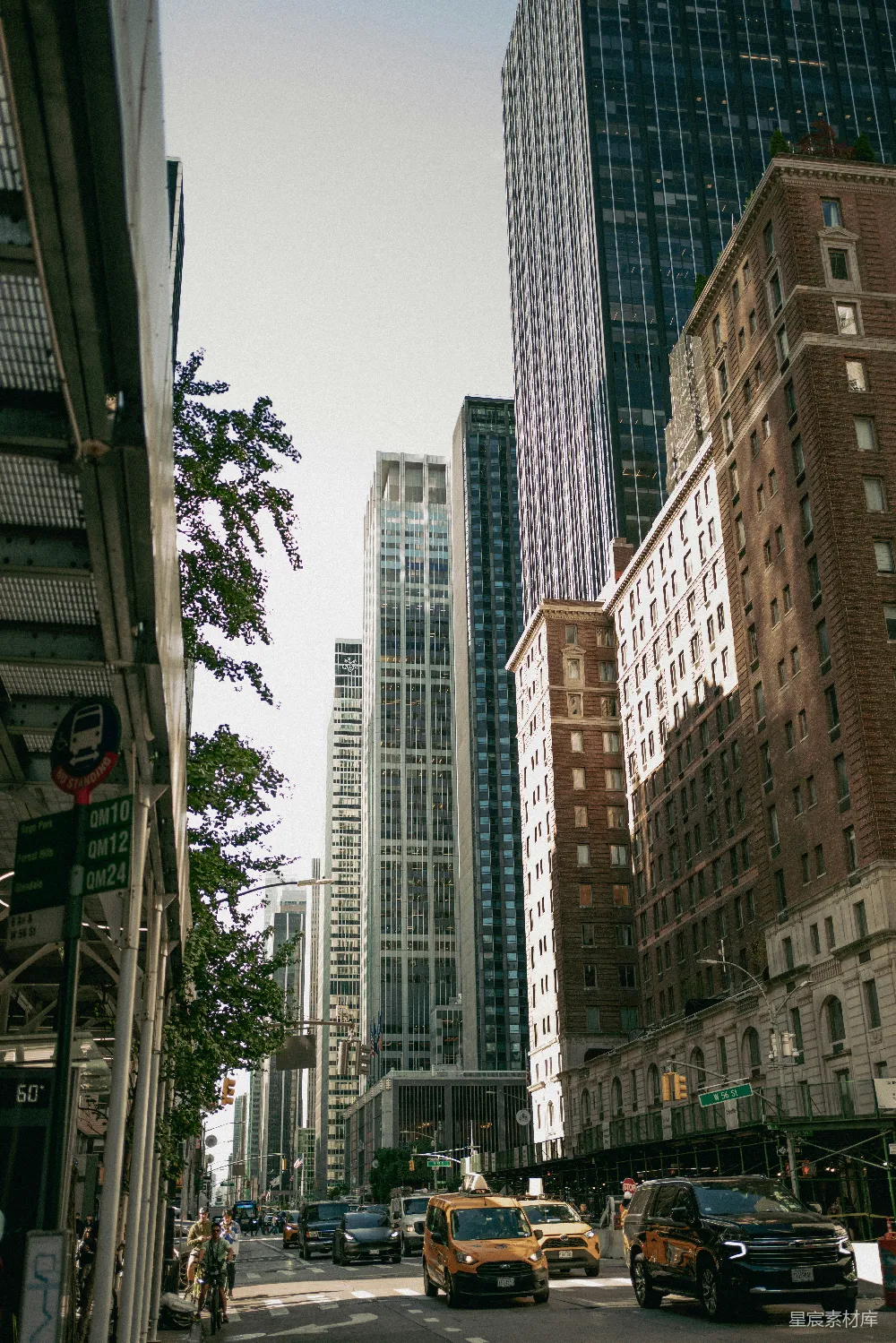 这张图片展示了一个繁忙的都市街道场景，高楼大厦林立，街道上车辆和行人穿梭，树木点缀其间，营造出一种充满活力的都市生活氛围。