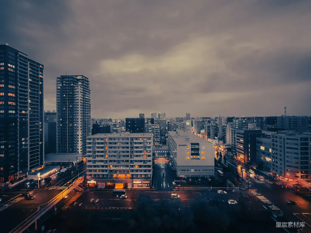 这张图片展示了一个城市的黄昏景色，天空中布满了云层，建筑物的灯光在夜幕降临前微微亮起。街道上车辆稀少，显得格外安静，给人一种平静而宁静的感觉。适合用于描述城市生活的静谧时刻，或者作为城市风光的背景素材。