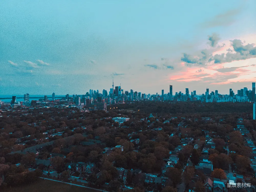 这张图片展示了城市的全景，夕阳的余晖洒在城市的天际线上，远处的天际线被染成了橙红色，近处的建筑和树木在蓝色的天空下显得格外宁静。整个画面给人一种平静而美丽的感受，适合用于城市风光、自然景观和旅行宣传的背景图片。