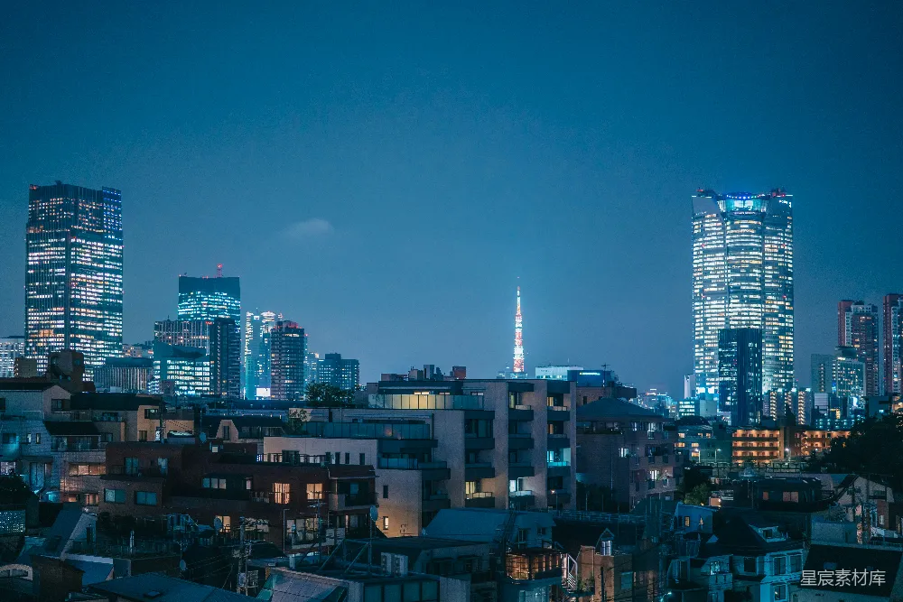 这张图片展示了东京的夜景，高楼大厦在夜色中灯火辉煌，背景中的东京塔在灯光的映衬下显得格外醒目。前排的低矮建筑与后方的高楼形成鲜明对比，展现出东京独特的城市景观。适合用于展示东京的现代化都市风貌，或者用作城市风光的背景素材。