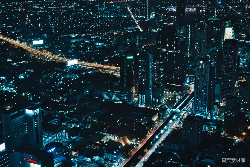 这张图片展示了夜晚的城市景象，高楼大厦灯火辉煌，道路两旁的灯光形成一道道光带，整体色调偏冷，给人一种宁静而繁忙的感觉。适合用于城市风光、夜景摄影、都市生活等主题。