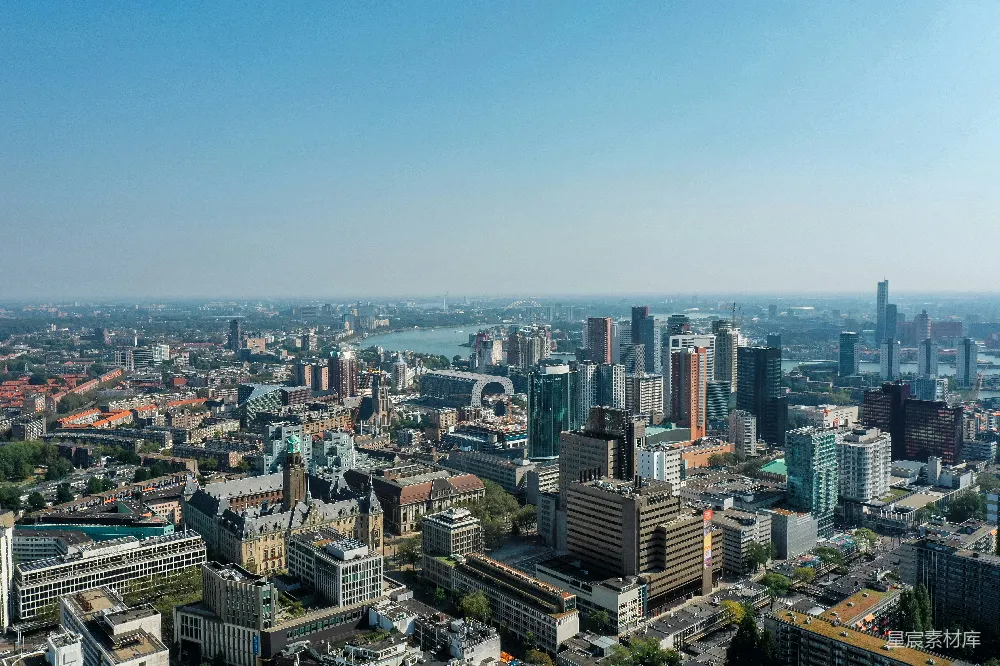 这张图片展示了荷兰鹿特丹的城市全景，从高空俯瞰可以看到各式各样的现代建筑和古老的教堂，中间的圆形建筑尤为显眼，背景是清澈的天空和远处的河流，体现了城市与自然的和谐共存。