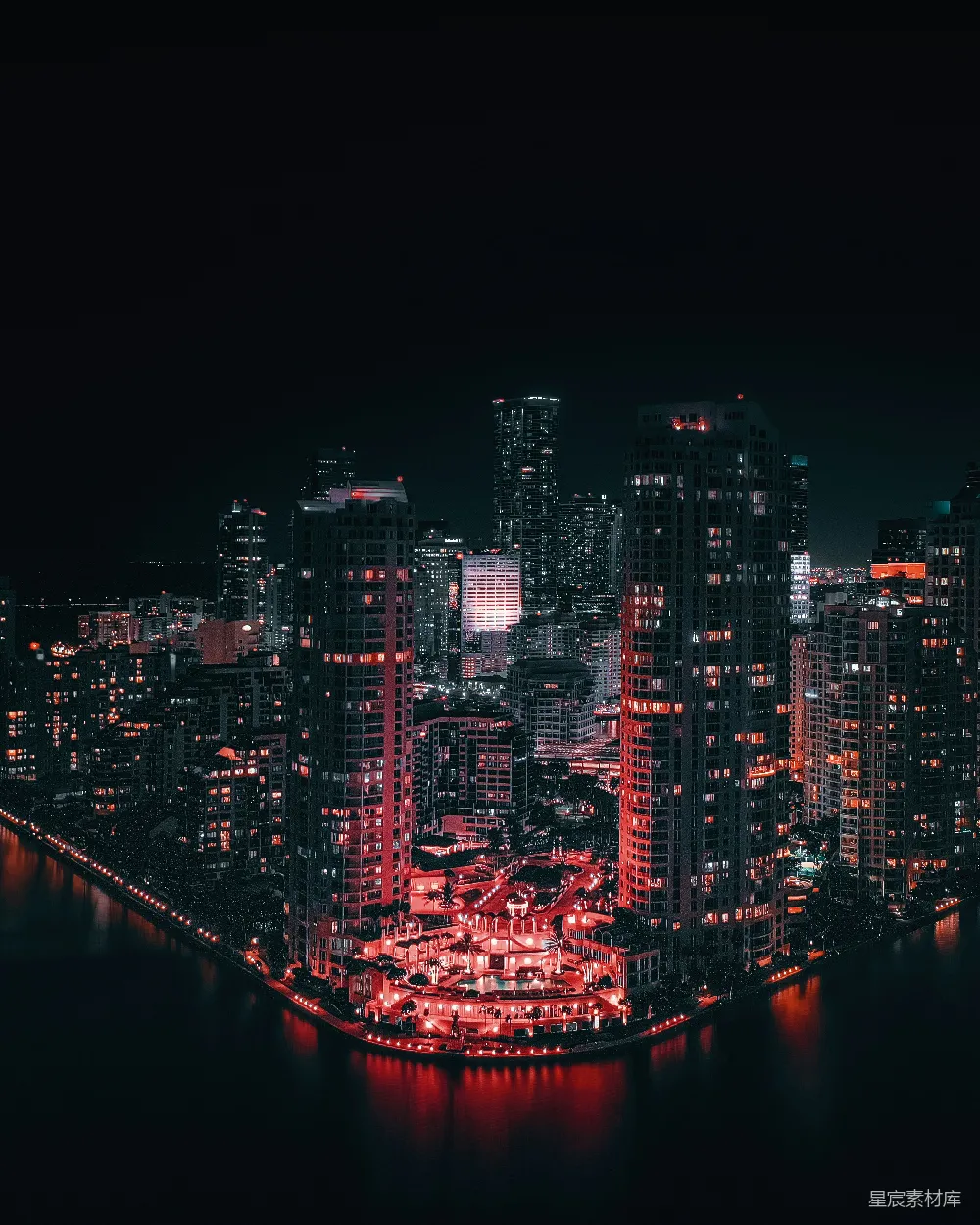 这张图片展示了夜晚的城市景观，高楼大厦在红色灯光的映衬下显得格外醒目，河流反射出城市的倒影，营造出一种静谧而神秘的氛围。适合用于城市夜景、建筑摄影或都市生活的主题背景。