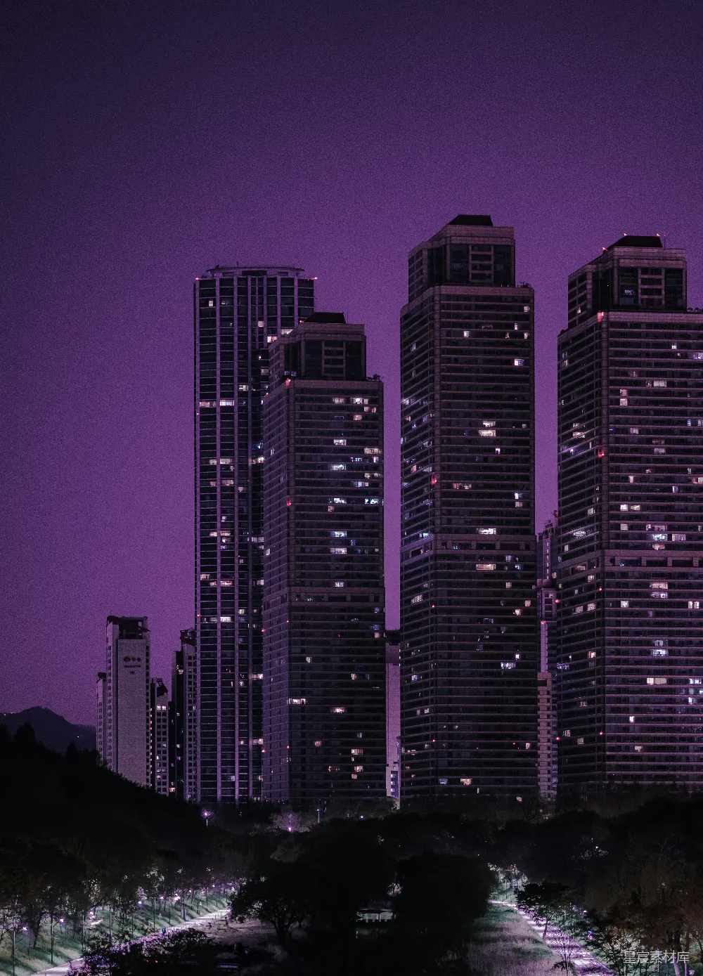 这张图片展示了夜晚中城市的剪影，高耸的建筑在紫色的天空下显得格外醒目。街道两旁的灯光与建筑的轮廓交织在一起，营造出一种宁静而神秘的氛围。适合用于城市夜景、现代都市、建筑摄影等场景。