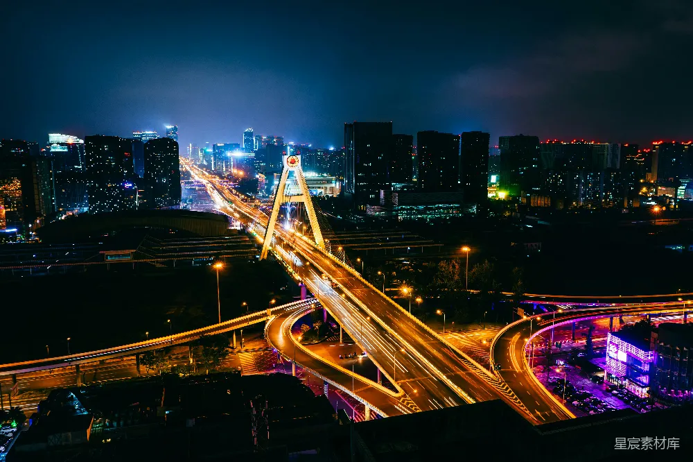 这张图片展示了一个城市的夜景，画面中央是一座现代化的桥梁，桥上的车流形成光带，展现出城市的繁忙与活力。背景是高楼大厦，灯光璀璨，远处的夜空显得宁静而深邃。整体风格现代且充满动感，适合用于城市宣传、旅游宣传或现代生活场景的展示。
