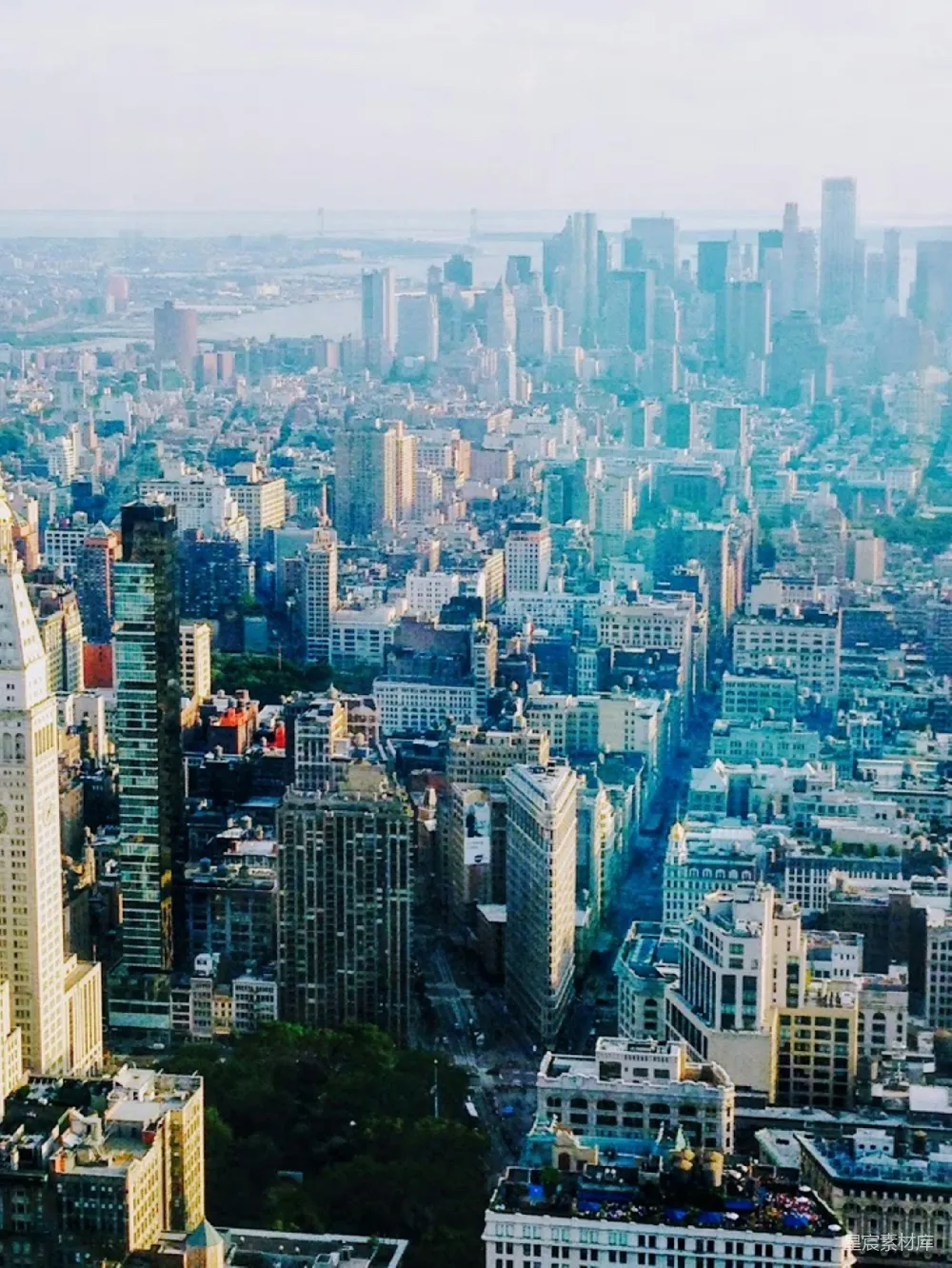 这张图片展示了纽约市的天际线，从高处俯瞰，可以看到密集的高楼大厦和宽阔的街道。天空呈现出柔和的蓝绿色，给人一种宁静而现代的感觉。适合用于城市风光、旅游宣传或城市生活展示。