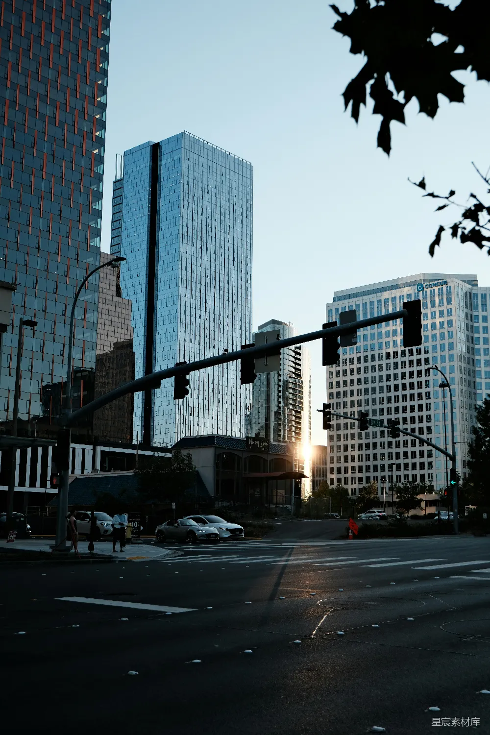 这张图片展示了城市中的一处街景，夕阳的余晖洒在高楼大厦和街道上，形成美丽的光影效果。远处的建筑物反射着夕阳的光芒，近处的街道上车辆稀少，显得宁静而美丽。适合用于城市风光、夕阳主题或现代都市生活的背景素材。