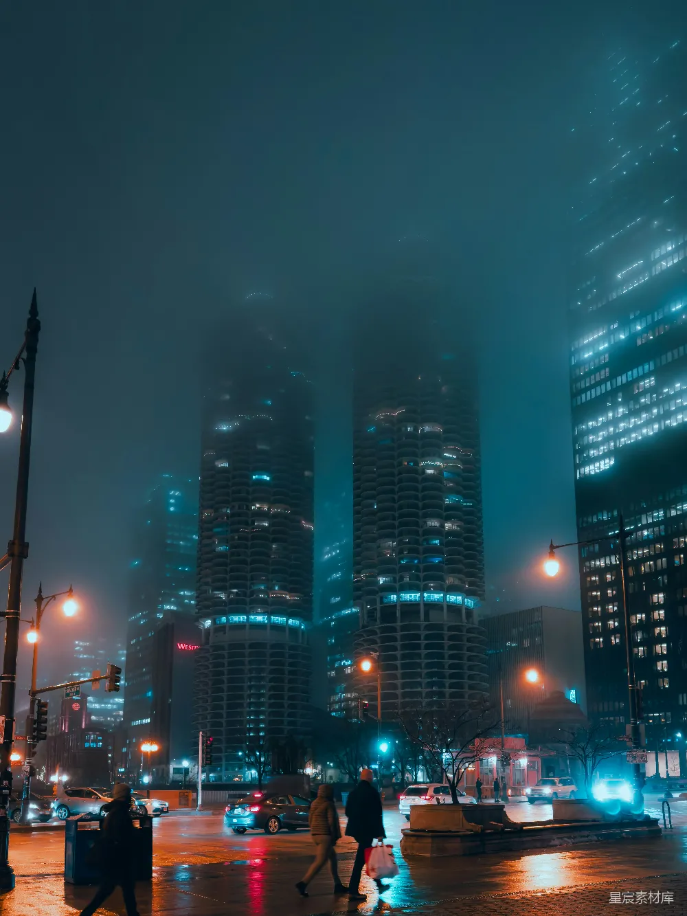 这张图片展示了一个雾蒙蒙的夜晚，城市中的高楼大厦在灯光的照耀下显得格外神秘。街道上行人匆匆，车流不息，营造出一种现代都市夜生活的氛围。天空中雾气弥漫，使得远处的建筑若隐若现，给人一种朦胧而宁静的感觉。