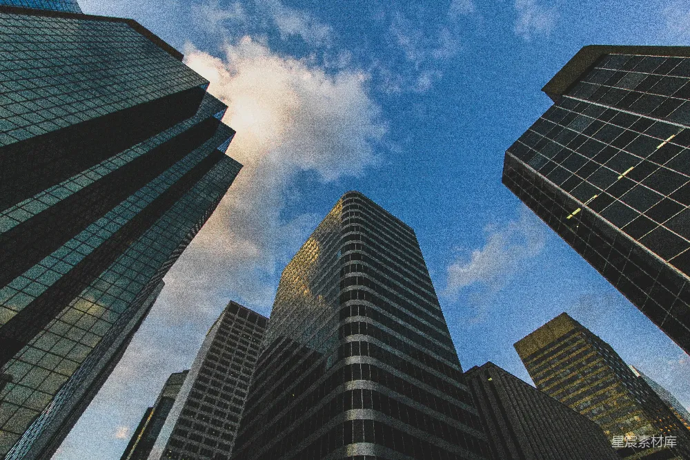 这张图片展示了从低角度仰望摩天大楼的景象，天空中飘着几朵白云，建筑物的玻璃幕墙反射着光线，给人一种宏伟和现代的感觉。适合用于城市、商务或现代风格的广告、海报或建筑展示。