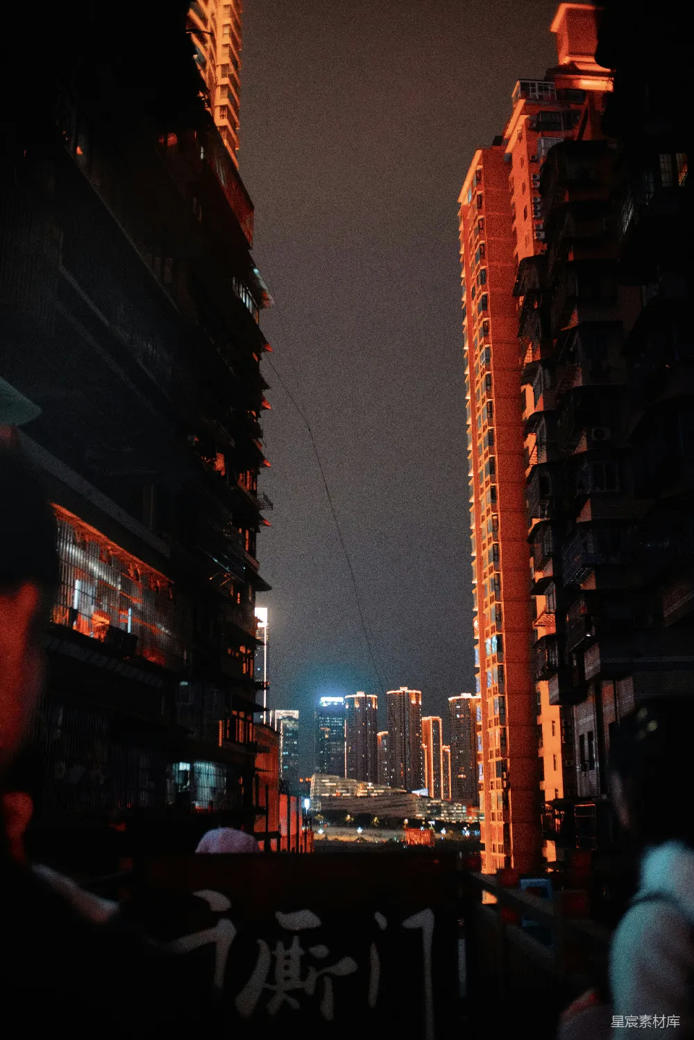 这张照片拍摄于夜晚的城市街道，两侧高楼林立，灯光昏黄，营造出一种静谧而神秘的氛围。画面中央的建筑上有一些模糊的文字，增加了画面的深度和故事性。适合用作城市夜景、建筑摄影或旅行宣传的素材。