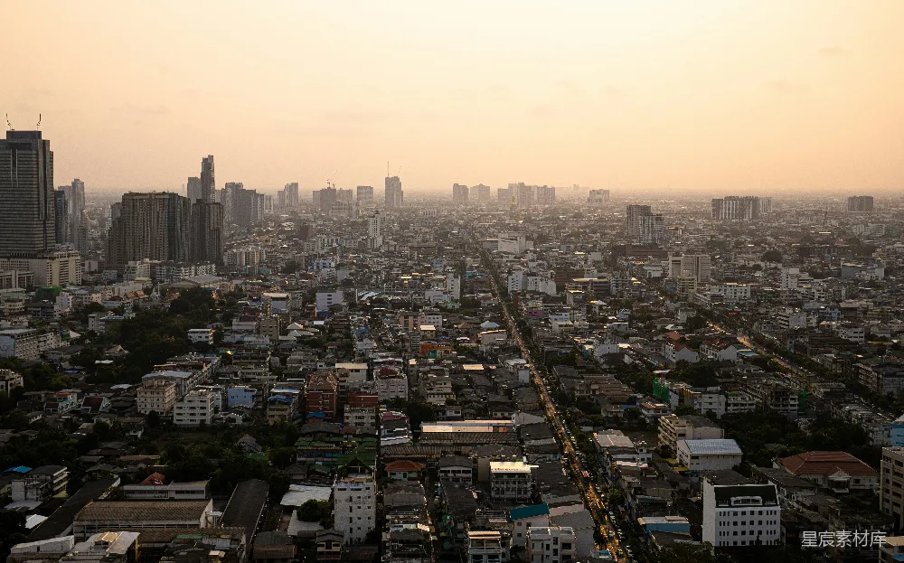 这张图片展示了夕阳下的城市全景，高楼大厦与低矮的住宅楼交织在一起，道路两旁的树木与建筑形成对比，营造出一种宁静而美丽的氛围。适合用于城市风光、旅游宣传或城市规划展示。