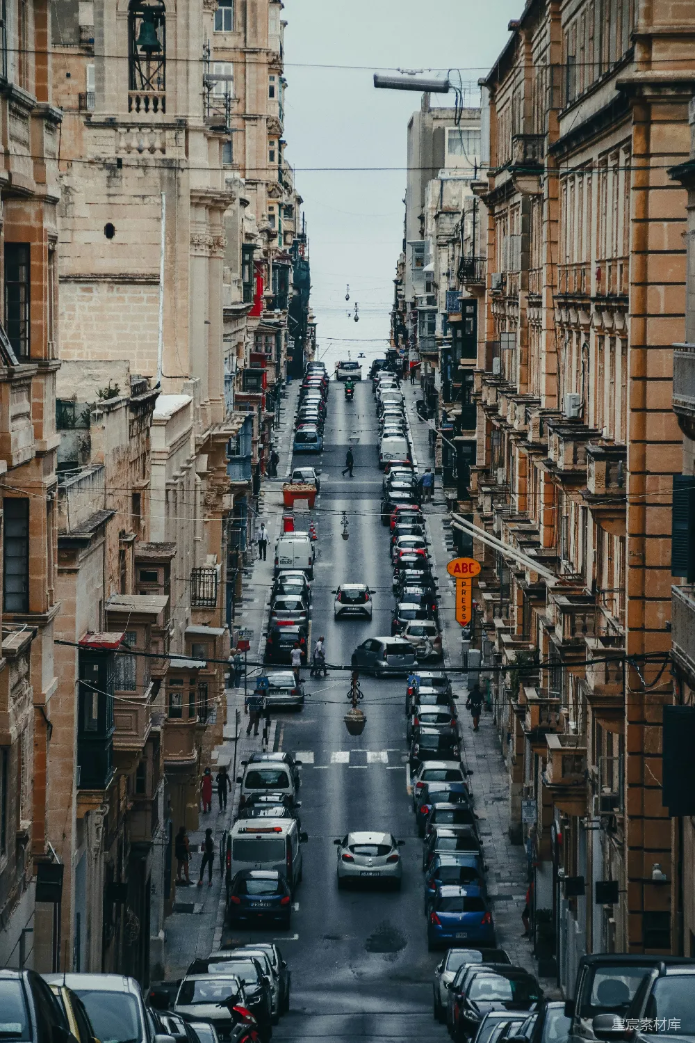 这张图片展示了欧洲一个老城区的街道俯瞰景象。两旁是古老的建筑，街道两旁停满了汽车，中间是行驶的车辆和行人。天空阴沉，给人一种略显压抑的感觉。适合用来展示欧洲城市的历史风貌和生活场景。