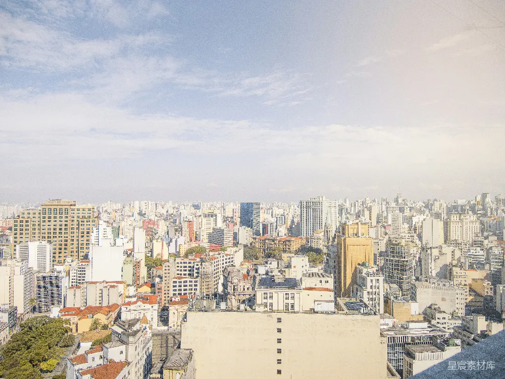 这张图片展示了城市全景，阳光洒在摩天大楼上，天空中飘着几朵云。画面中既有现代化的高楼大厦，也有低矮的住宅楼，展现了城市多样化的建筑风格。适合用于城市风光、旅游宣传或建筑设计的背景素材。