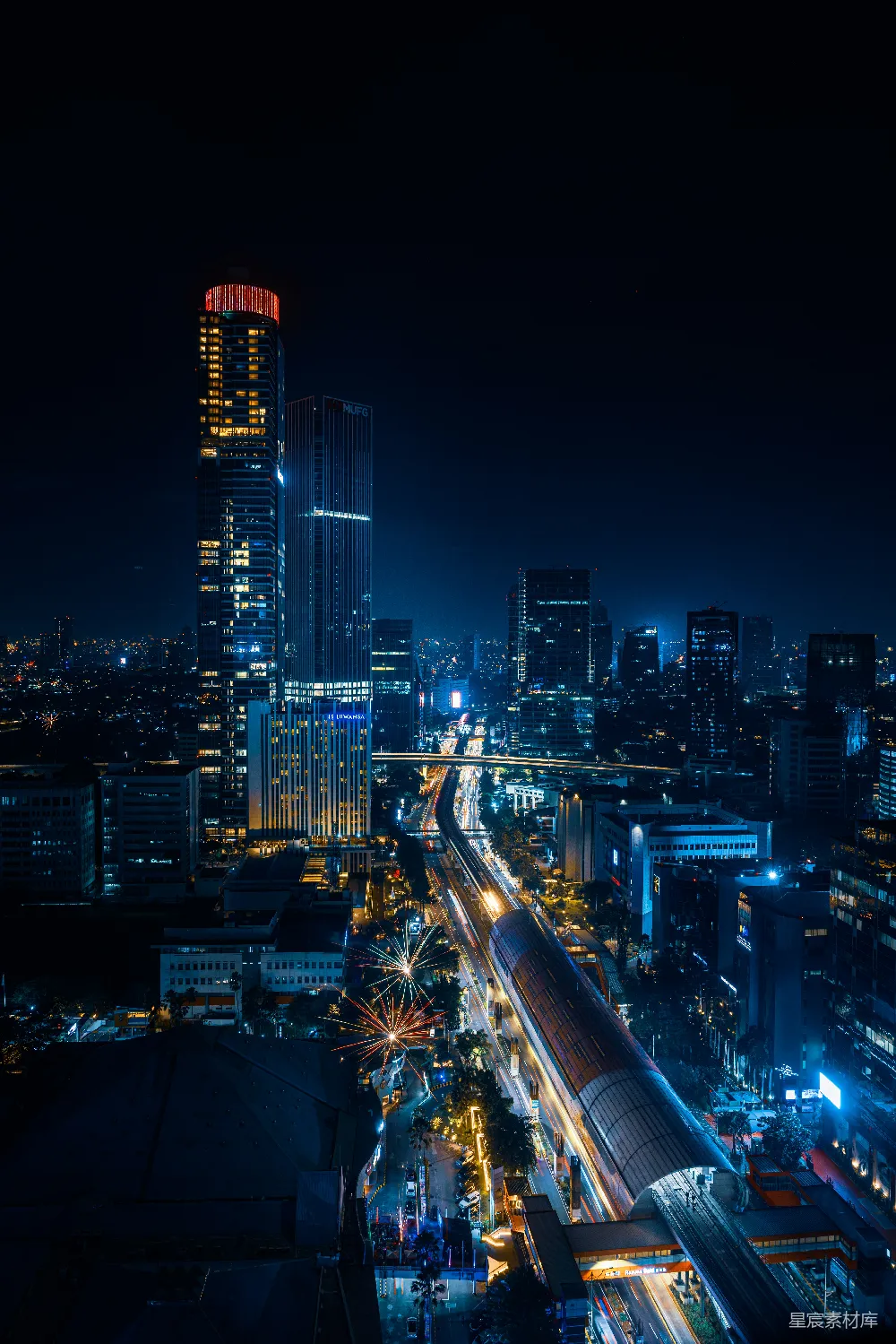 这张图片展示了夜晚城市的壮观景象。高楼大厦在夜色中散发出温暖的光芒，道路上的车流形成一道道光带，远处的烟花在夜空中绽放，增添了节日的气氛。整体色调以蓝色和黄色为主，营造出一种宁静而又充满活力的氛围。这张图片适合用作都市夜景、城市风光或节日庆