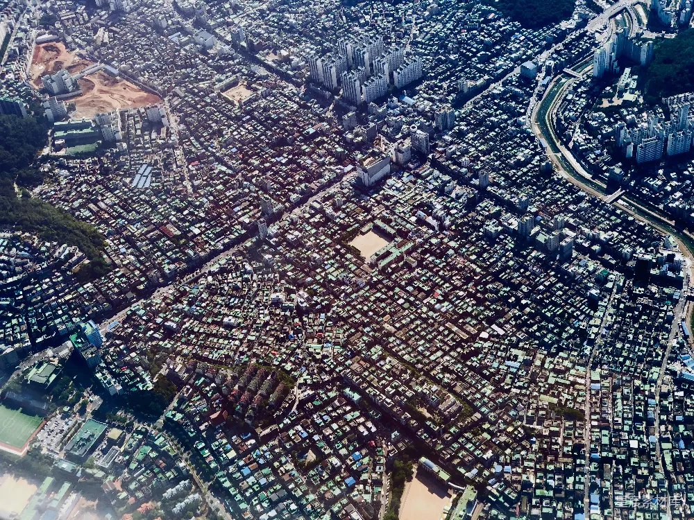 这张图片展示了从高空俯瞰的城市景象，密集的住宅区构成了城市的核心。建筑群排列整齐，道路交织形成网格状，显示出城市规划的有序性。周围有少量的绿地和大型建筑，体现了城市功能区的划分。整体风格现代而紧凑，适合用于城市规划、建筑设计或地理信息的展示