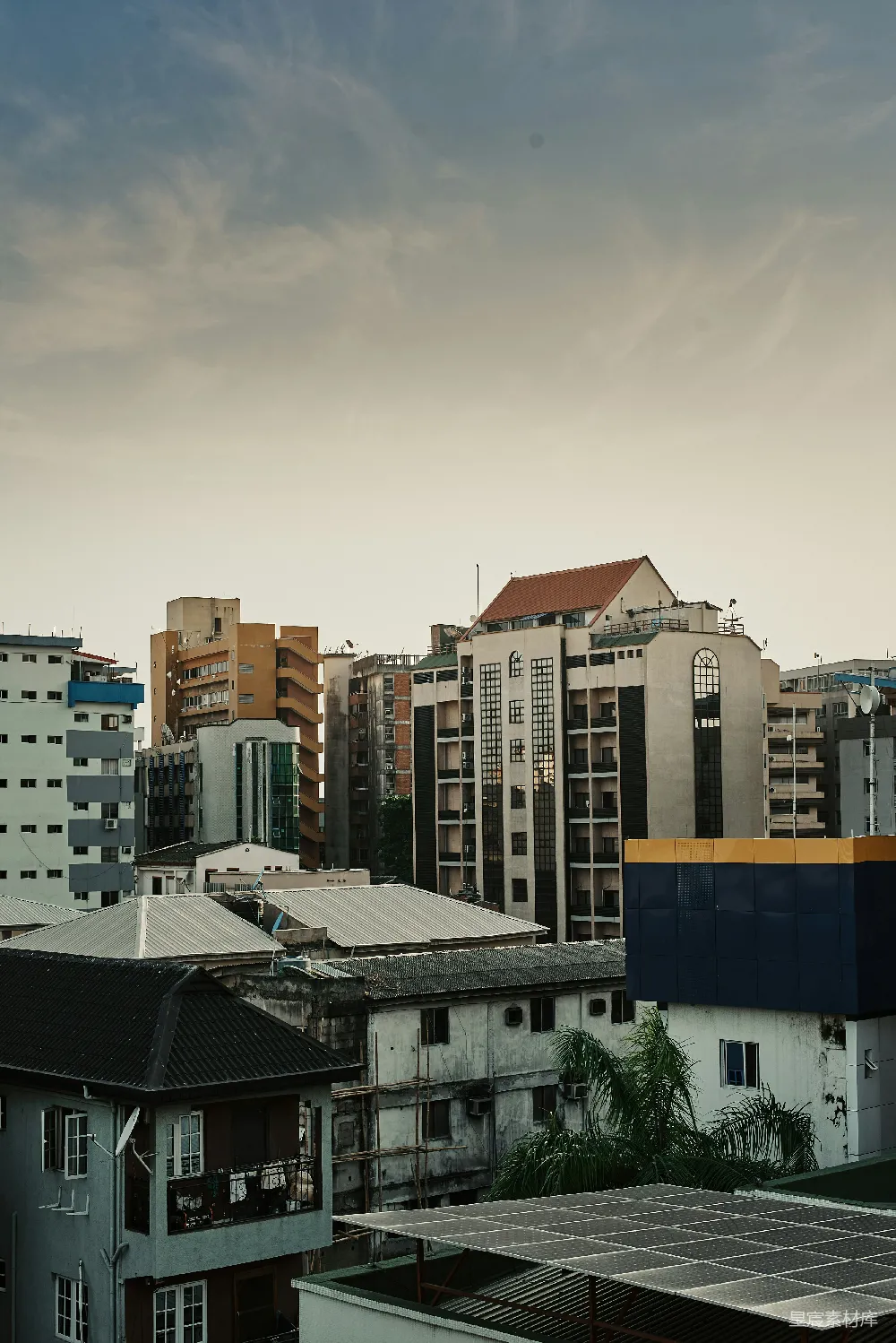 这张图片展示了一片城市的天际线，多样的建筑物在夕阳的映衬下显得格外生动。低矮的住宅楼与高耸的现代建筑交相辉映，展现出城市的多样性和活力。天空中飘着淡淡的云彩，为整个画面增添了几分宁静与美感。适合用于城市风光、建筑摄影或城市生活主题的设计素材