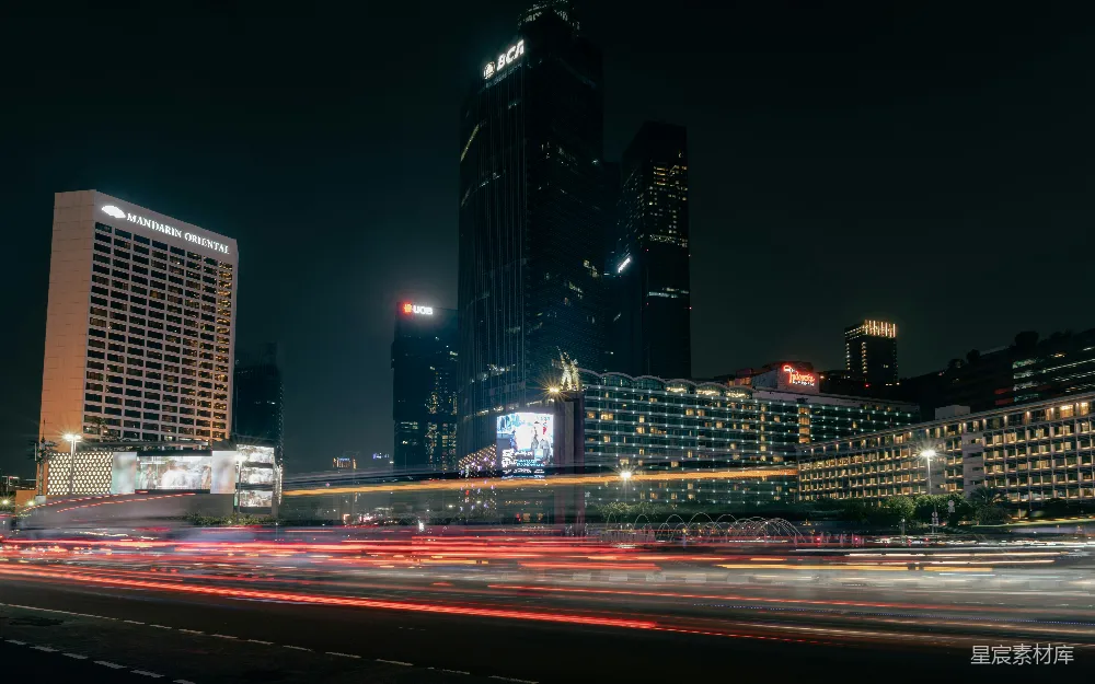 这张图片展示了繁忙都市的夜景，高楼大厦灯火辉煌，街道上车流如织，形成一道道光带。建筑物的灯光与街道上的车灯交织在一起，营造出一种现代都市的繁华氛围。适合用作城市夜景、现代都市、交通繁忙等主题的背景图片。