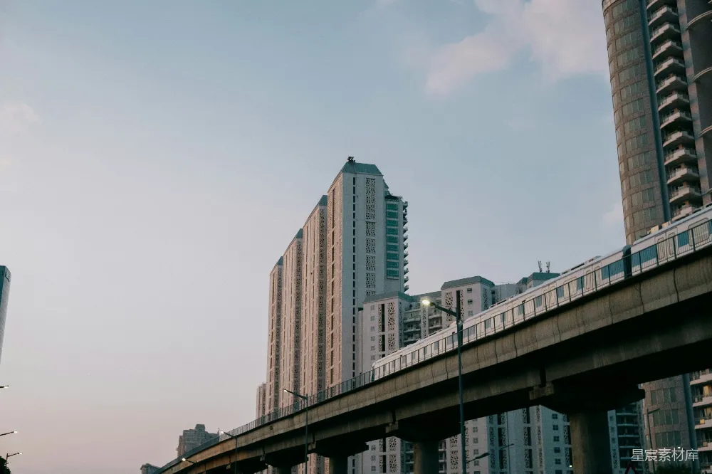 这张图片展示了现代化城市中的高架列车，背景是高耸的建筑群，天空呈现出柔和的色彩，给人一种宁静而现代的感觉。高架桥的设计不仅节省了地面空间，也为城市增添了独特的视觉元素。适合用于城市建筑、现代交通或城市风光的展示。