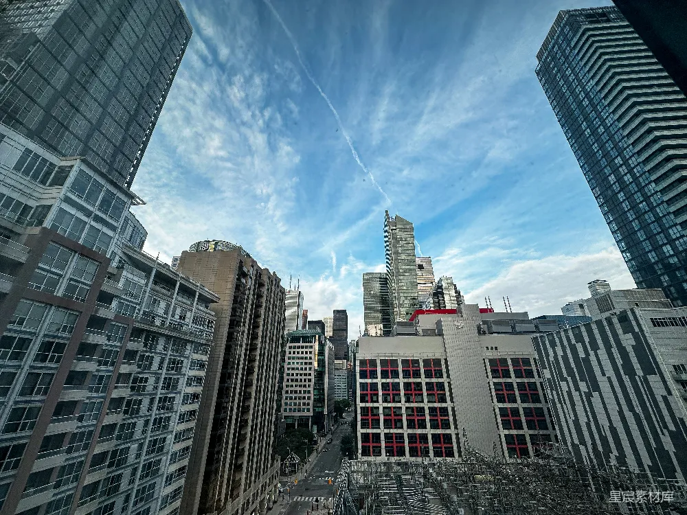 这张图片展示了城市中心的高楼大厦，天空中飘着几朵白云，给人一种现代都市的感觉。建筑物错落有致，玻璃幕墙反射着蓝天，给人一种繁忙而充满活力的感觉。适合用于城市建筑、都市生活或现代都市风格的素材。