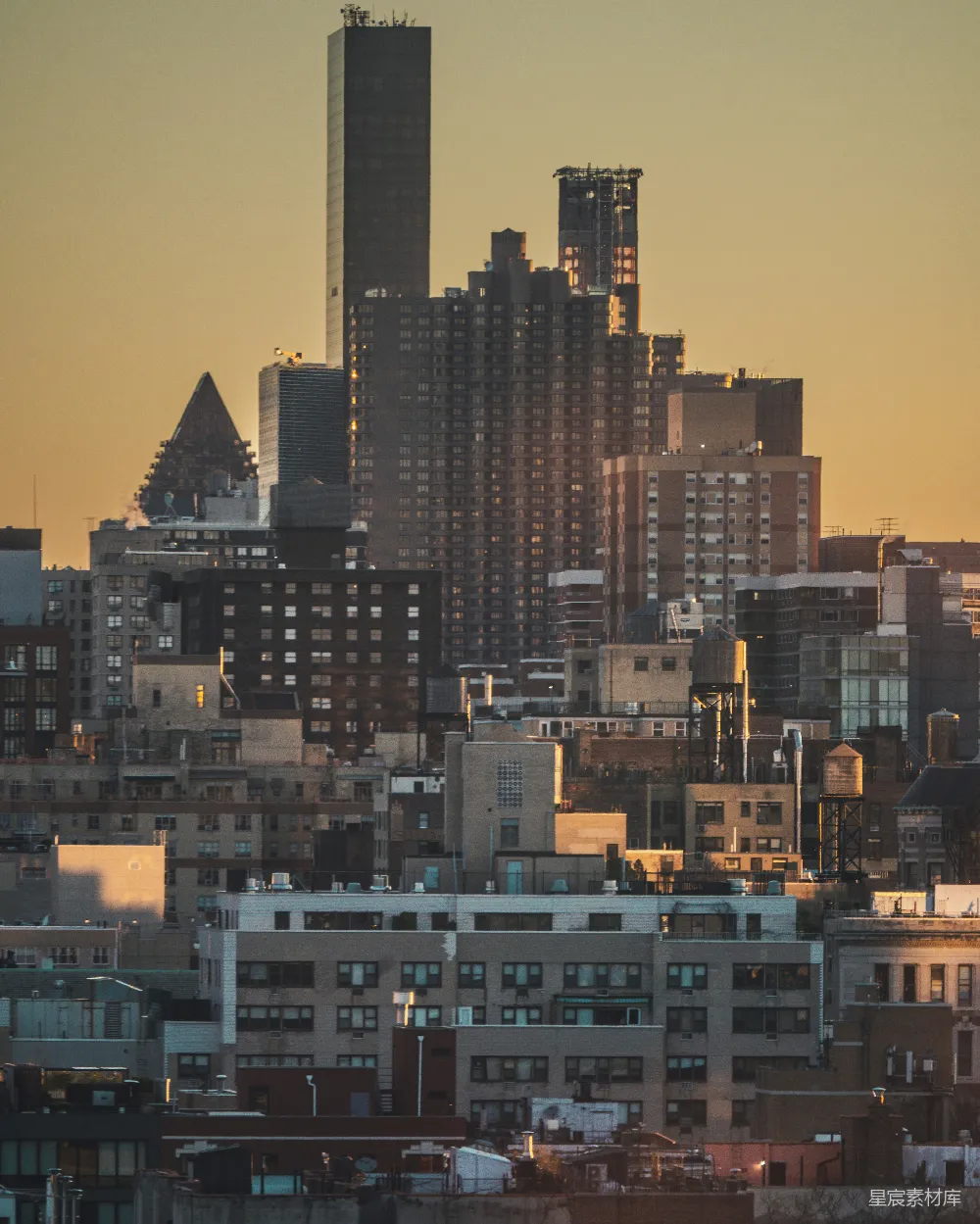 这张图片展示了纽约市在夕阳余晖下的天际线，高楼大厦在金色的阳光下显得格外醒目。近处的建筑层次分明，远眺的摩天大楼在夕阳的映衬下显得尤为壮丽。这幅画面捕捉了城市生活的繁忙与宁静，适合用于城市风光、旅游宣传或建筑设计相关的背景素材。
