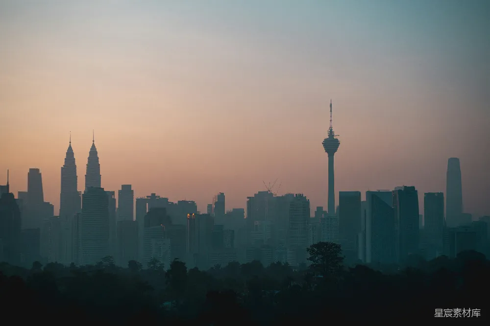 这张图片展示了日落时分的城市剪影，天空被染成了温暖的橙色和紫色，远处的高楼大厦在夕阳的映衬下显得格外壮观。前景中的树木在剪影中显得更加柔和，为整个场景增添了一丝自然的元素。这张图片适合用于城市风光、旅游宣传或都市生活主题的背景素材。