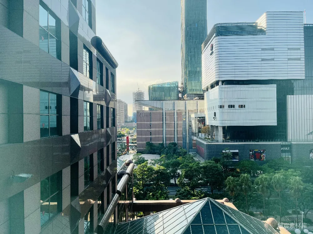 这张图片展示了一个现代化城市的景观，高楼大厦错落有致，玻璃幕墙反射着蓝天白云。前景中可以看到一些建筑的局部，而远处则是高楼大厦和绿地，展现了都市的繁华与自然的和谐共存。适合用于城市风光、商务宣传或都市生活的展示。