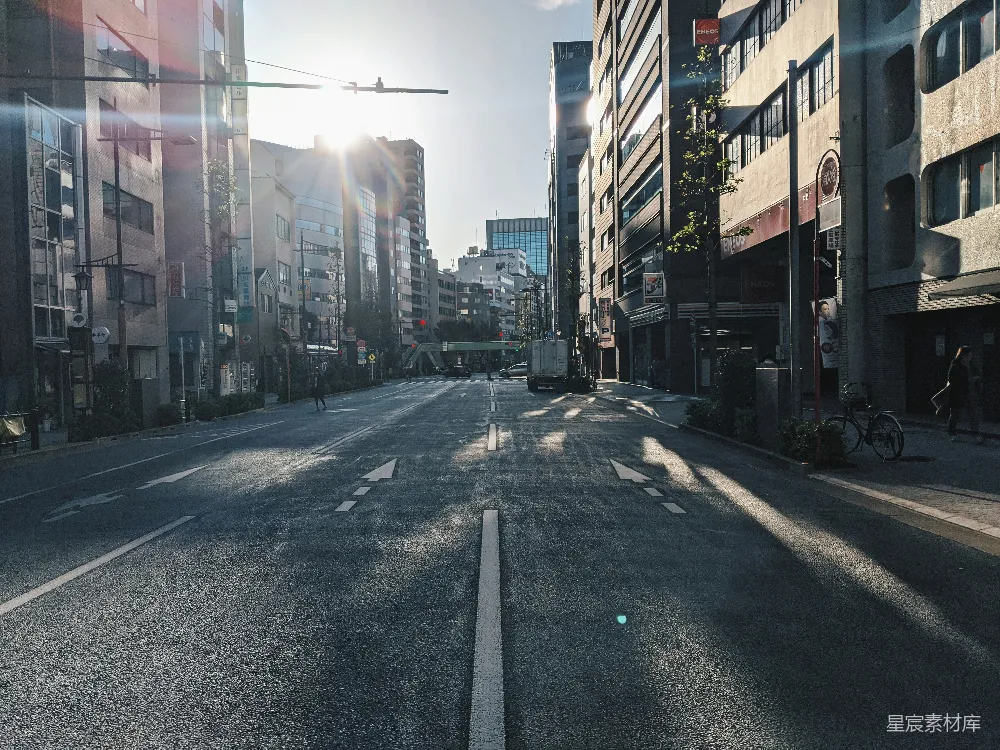 这张图片展示了一条城市的街道，阳光透过高楼的缝隙洒在路面上，形成斑驳的光影。街道两旁是现代化的建筑，显得宁静而有序。适合用于城市生活、自然光与城市结合的背景图片。